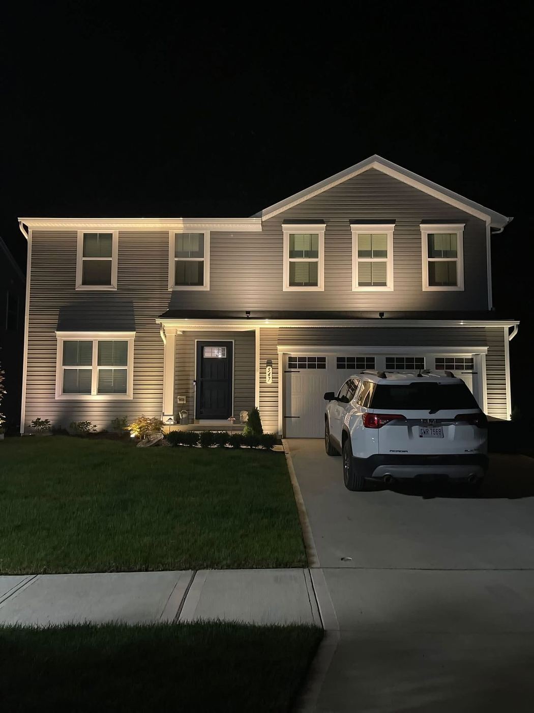 Warm landscape uplighting illuminating a two-story home's facade and entryway at night