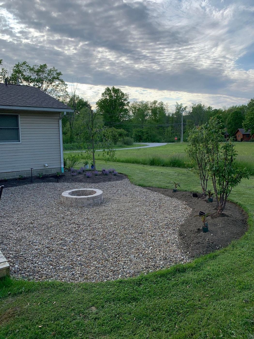 Gravel fire pit patio with freshly mulched planting bed and new trees installed by Campbell's Lawn Care