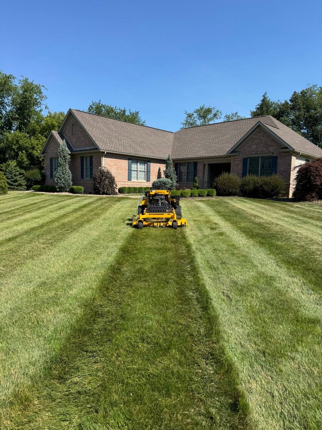 Campbell's Lawn Care zero-turn mower cutting clean stripes into a brick home's front lawn